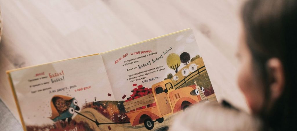 A mother and toddler sharing a story from an illustrated children's book indoors.
